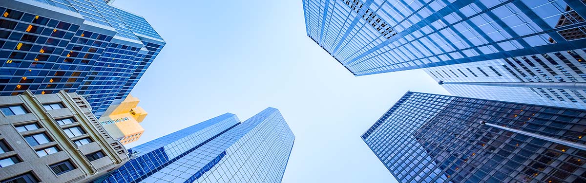 looking up at a group of modern skyscrapers against a clear blue sky.