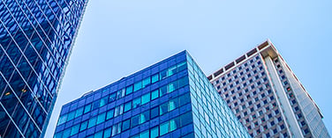 Low-angle view of modern glass skyscrapers against a clear blue sky.