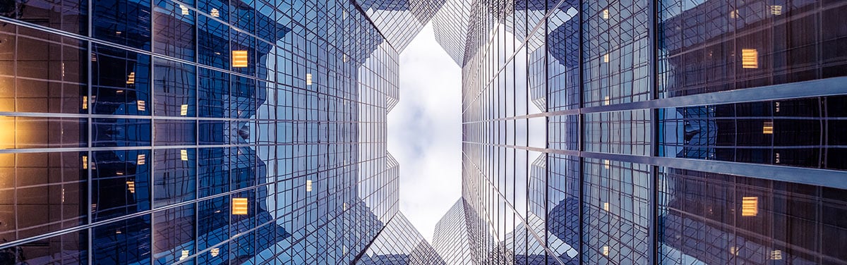 An upward looking view of towering glass office buildings creating a symmetrical, geometric pattern against the sky.