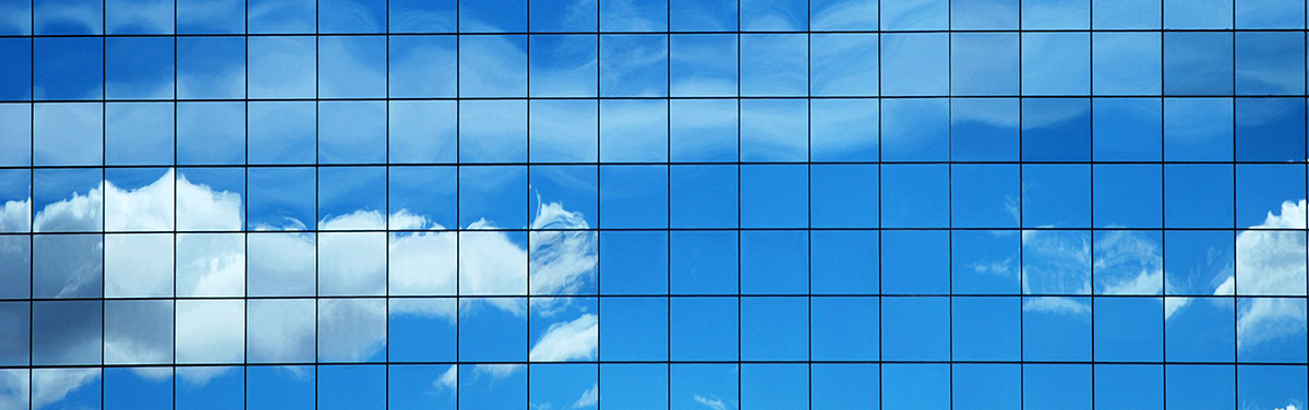 grid of square windows on an office building reflecting a blue sky with fluffy white clouds